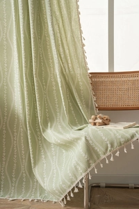 Close-up of light green kitchen curtain with white floral print and cream tassel edges