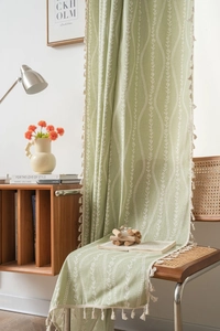 Detail of light green floral curtain with white vine patterns and elegant cream tassels