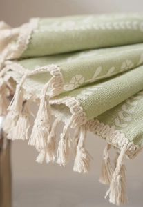 Close-up of light green kitchen curtain featuring white floral print and woven tassel fringe