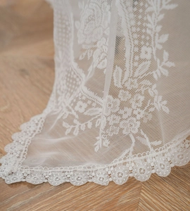 Close-up of intricate floral lace tablecloth with elegant scalloped edges on wood floor