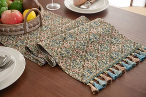 Detailed view of jacquard floral table runner with blue and brown tassels on dark wood