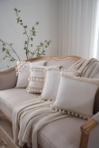 Close-up of bohemian cream cotton linen cushion covers with decorative tassels on a sofa