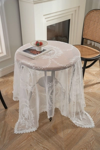 Detail of white round lace tablecloth featuring intricate floral embroidery on wooden table