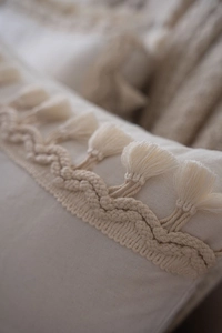Close-up of bohemian cream pillow cover featuring intricate woven bands and fringe tassels
