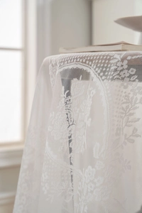Close-up detail of white lace tablecloth with floral embroidery and scalloped edges