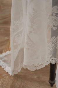 Close-up of white lace tablecloth with floral embroidery and wavy scalloped edges