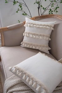 Detail view of bohemian cream throw pillow cover featuring woven ropes and fringe tassels