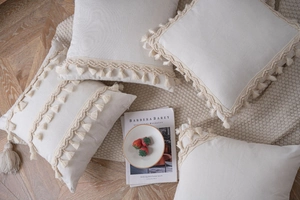 Detail of four beige textured cushion covers with fringe tassels on a wooden floor