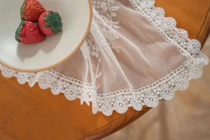 Detailed view of white floral lace tablecloth with intricate embroidery and cutout borders