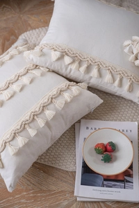 Close-up of beige boho pillow cover with woven textures and tassel fringe details