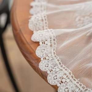 Modern white lace tablecloth with floral hollow patterns draped on a wooden table edge