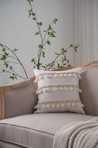 Close-up of bohemian cream throw pillow cover featuring woven lace and tassel details