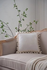 Close-up of cream square pillow cover with elegant woven fringe and tassel details