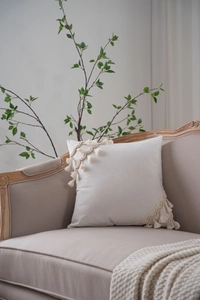 Detailed view of bohemian ivory cushion cover with handmade tassels on soft fabric