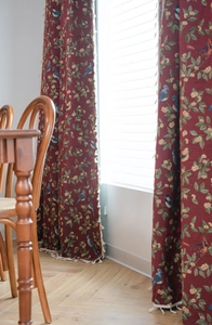 Detail of red floral and bird jacquard curtain with white tassel fringe in a sunlit room