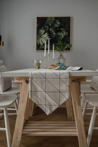 Detail eines beigen Tischläufers mit schwarzen geometrischen Dreiecken auf Holztisch
