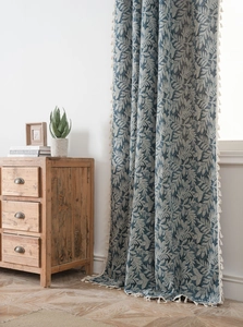 Close-up of blue boho curtain featuring white leaf patterns and beige tassel fringe edge