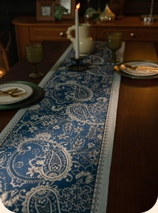 Detail of blue paisley jacquard table runner on wooden table with elegant dinnerware