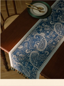 Detail of blue paisley jacquard table runner with decorative tassels on wooden table
