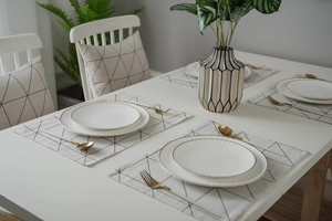 Detail eines geometrischen Tischläufers mit passenden Keramiktellern und Besteckset