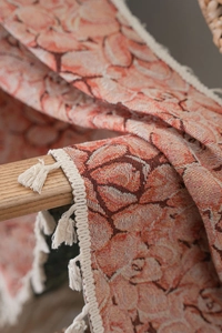 Detail of pink jacquard fabric with floral patterns and cream woven tassels on a chair