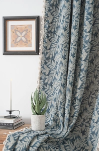 Detail of blue leaf pattern woven fabric with white fringe tassel trim on the curtain edge