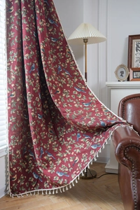 Detail of red vintage jacquard curtain with bird pattern and cream tassels on leather sofa