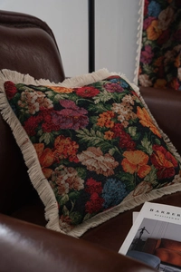 Close-up of vintage floral tapestry pillow with cream fringes on a brown leather chair