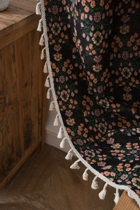 Detail of floral black jacquard woven curtain with decorative white fringe tassels