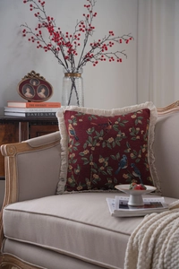 Detail of red jacquard throw pillow with bird flower pattern and cream fringe edges