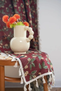 Detail view of red jacquard fabric featuring floral bird patterns and white cotton tassels