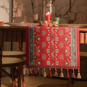 Detail of red geometric jacquard table runner with multi-color handmade tassels on wood table
