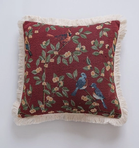 Detail of red jacquard pillow featuring woven birds and cream-colored fringe edges