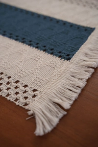 Detailed macro view of navy and beige woven table runner featuring tassels and openwork