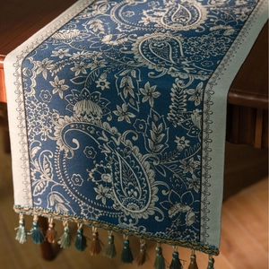 Close-up of blue paisley jacquard table runner with decorative tassels on wooden table