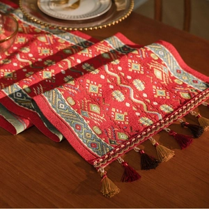Detail of red jacquard table runner with geometric patterns and colorful tassels