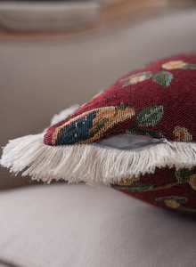 Macro view of red jacquard pillow with floral bird pattern and white fringe tassel