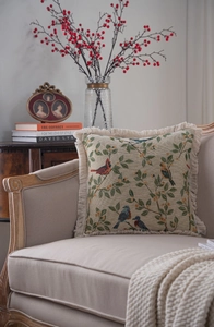 Detail of jacquard throw pillow with bird and leaf patterns and fringed edges on sofa