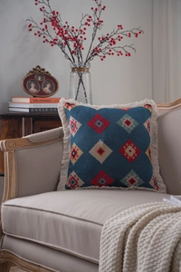 Detailed view of bohemian square pillow with blue diamond patterns and white tassels on sofa