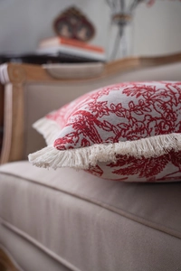 Detailed close-up of red floral jacquard cushion cover with white fringe trim on a chair
