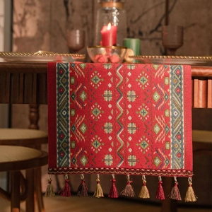 Traditional red table runner with jacquard geometric patterns and tassels on wooden table