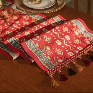 Red table runner with geometric jacquard pattern and elegant tassels on dark wood table
