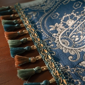 Blue Paisley jacquard table runner with decorative tassels on a dark wood surface