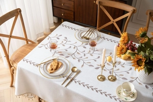 Dettaglio della tovaglia in lino beige con ricamo a rami e frange con piccoli pompon