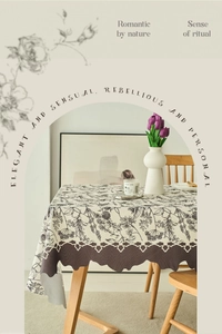 Detail of cream rectangular tablecloth with black floral print and scalloped edges
