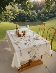 Dettaglio di ricamo floreale e nappe beige su tovaglia in lino color crema all'aperto