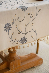 Dettaglio di ricami floreali e frange con nappe su tovaglia di lino beige