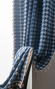 Detailed close-up of blue and white checkered jacquard fabric with cream tassel fringe