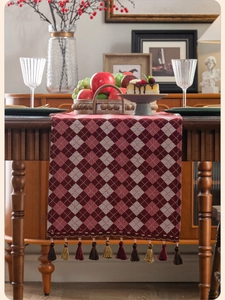 Detailed view of red and blue argyle table runner with luxury tassel fringe on wood table