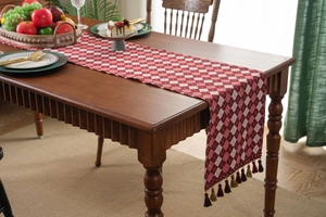 Detail of red and white checkered table runner with decorative tassels on wooden table
